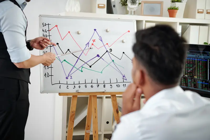 A man pointing at a line chart on an easel while a colleague looks on