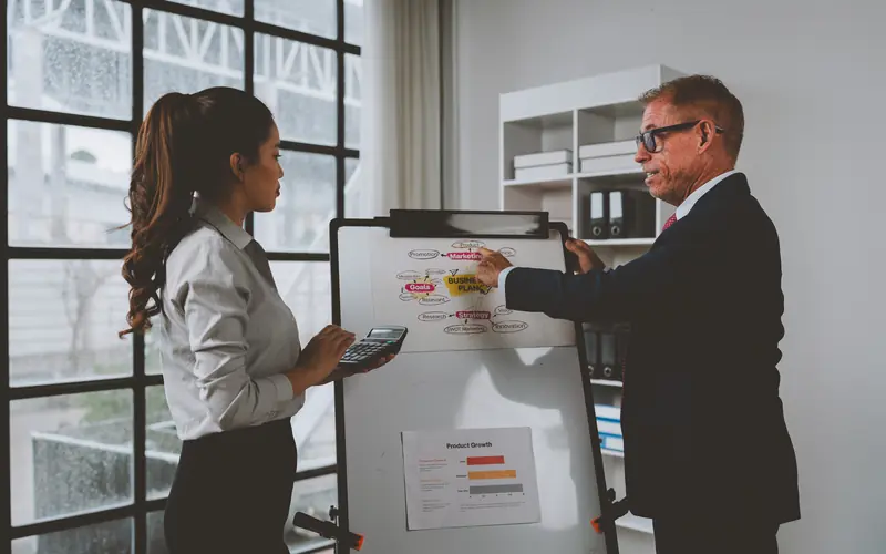 A man and a woman reviewing charts on a flip chart stand in an office